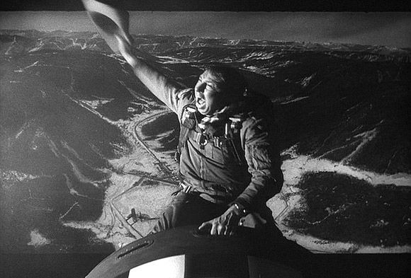 Still image from movie dr strangelove. Pilot dressed as a cowboy riding a nuclear bomb like a rodeo horse as it plummets towards detonation 