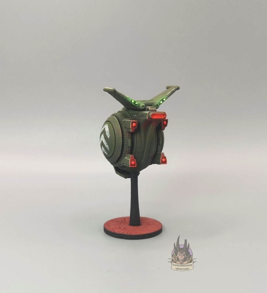 Drone - it's spherical with stablising fins at the top, in a drab green with grey chevron patterns on the side panels -back right view
