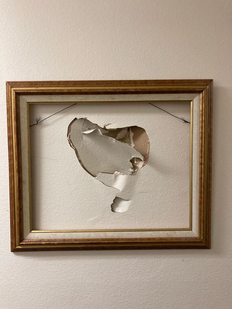 Wall of the lobby of an apartment complex. It’s a punched hole in the drywall with a gilded frame hung on it.