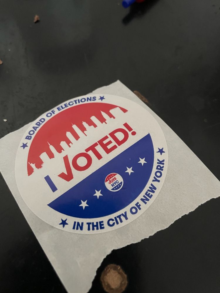 An NYC "I Voted!" sticker on a black desk.
