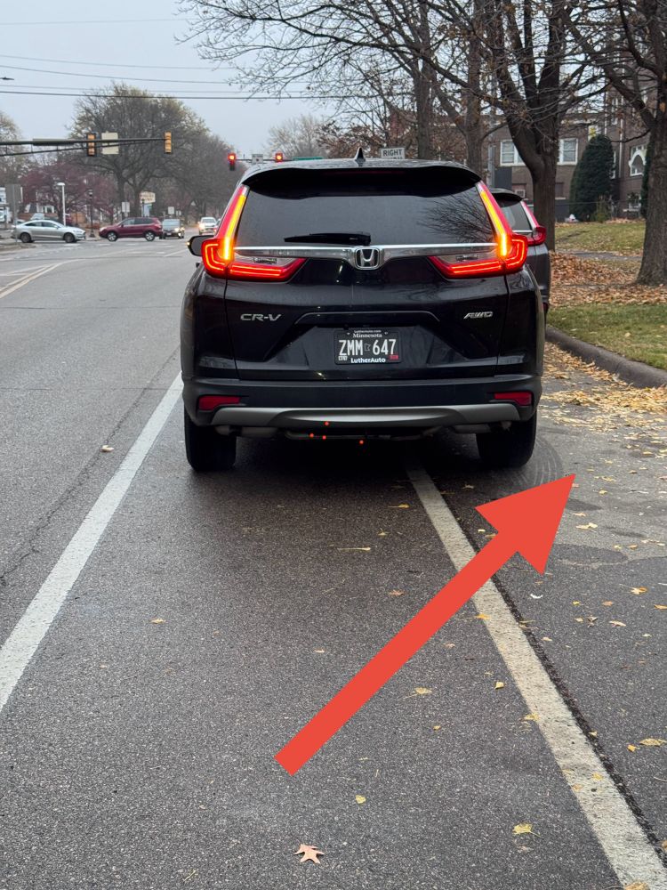 A car is parking the bike lane with a large red arrow pointing to an available parking spot directly next to the car parked in the bike lane
