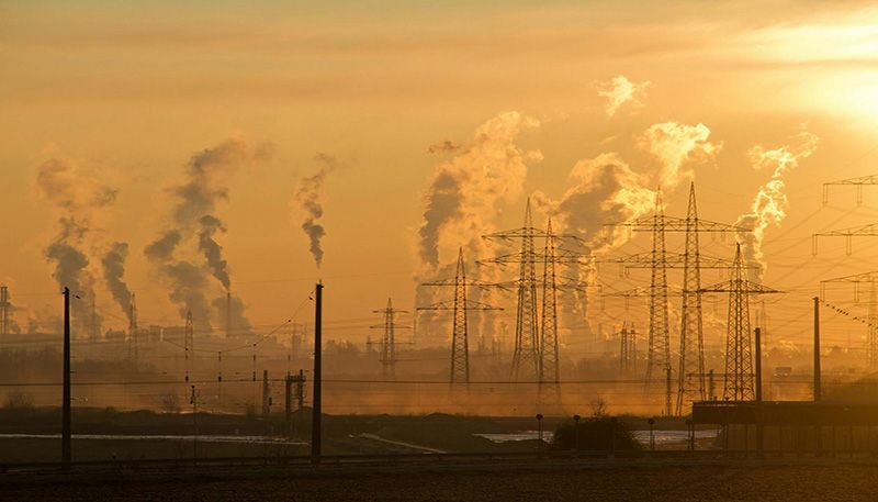 A large industrial area featuring power lines emitting smoke against a cloudy sky.