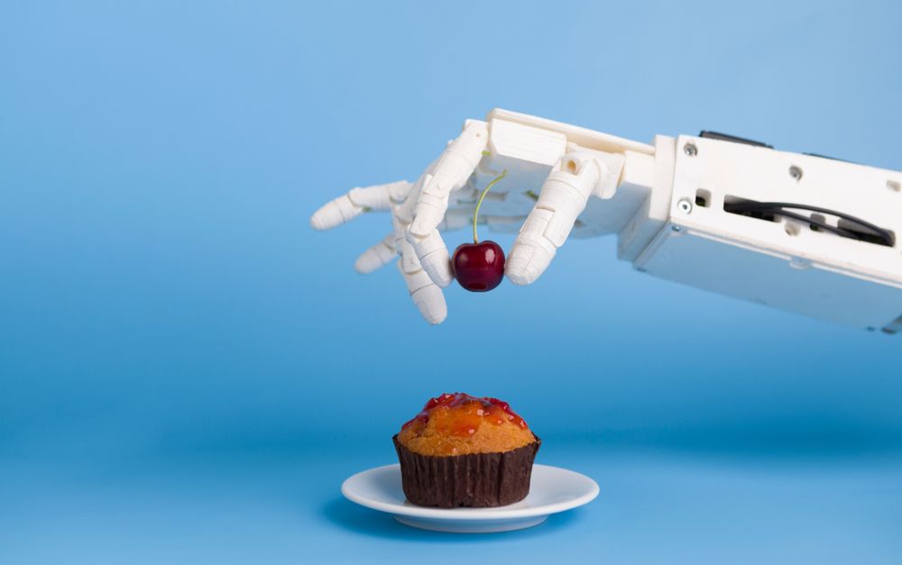 A robot hand places a cherry on the top of a cupcake. Stock photo. 