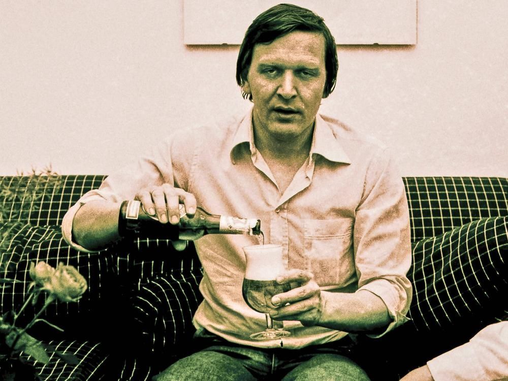 Altes Foto vom jungen Schröder. Er sitzt auf einer Couch, schenkt sich ein Bier ein und schaut mit starren, fast schon abwesend wirkenden, leeren Blick in die Kamera