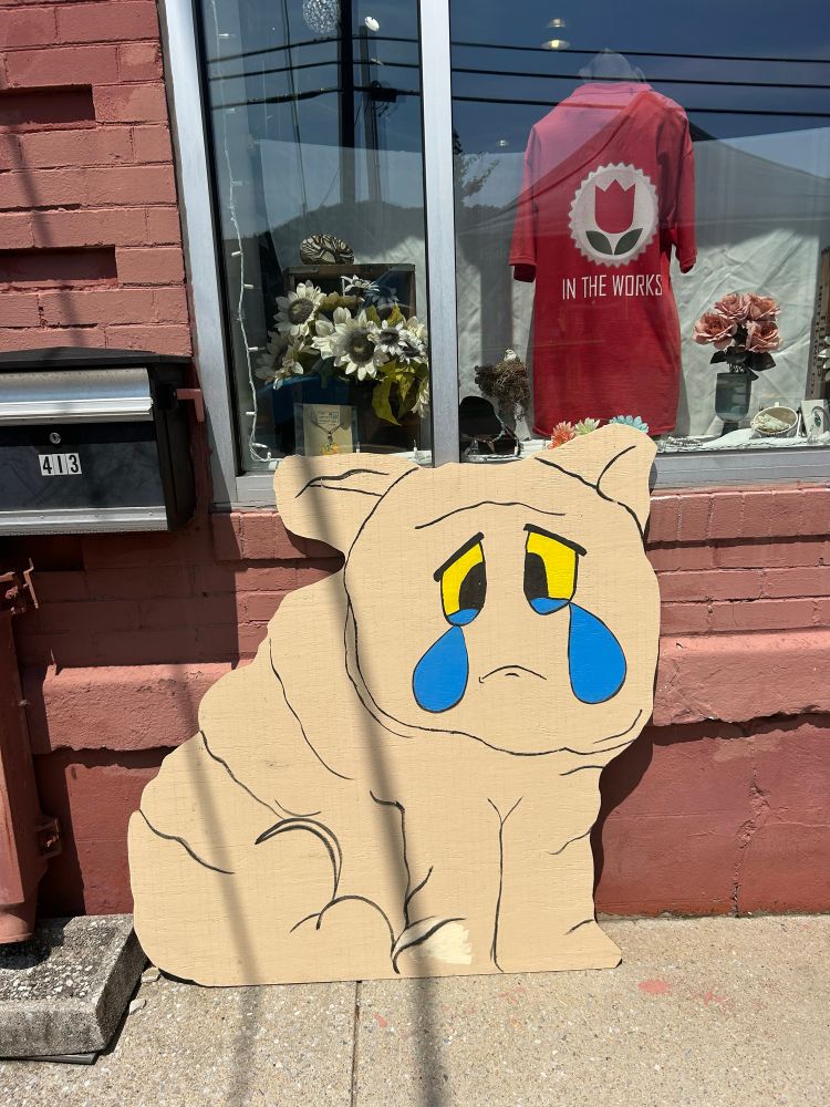 A wooden standee of the Squonk, a creature shaped similarly to a pig with wrinkly skin and big blue tears. 