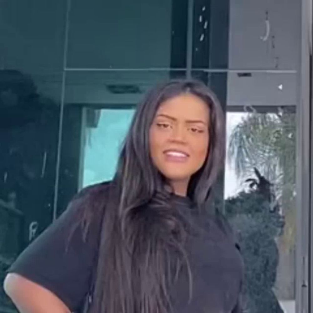 a woman with long black hair and a black shirt is standing in front of a glass door .