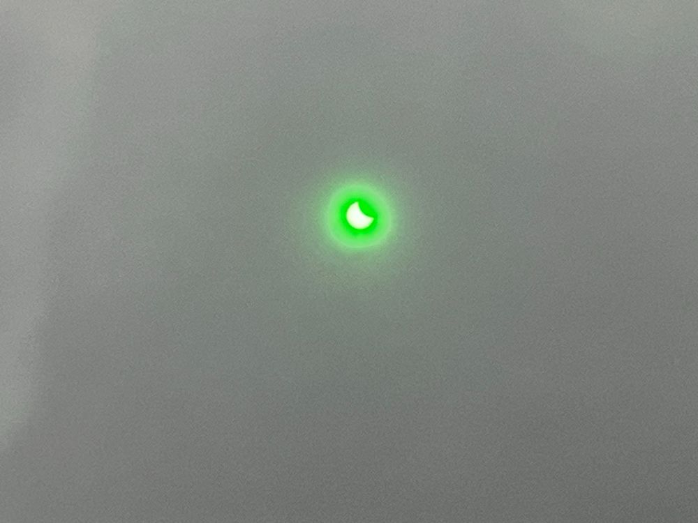 An image of the partial solar eclipse through a green tinged sun filter