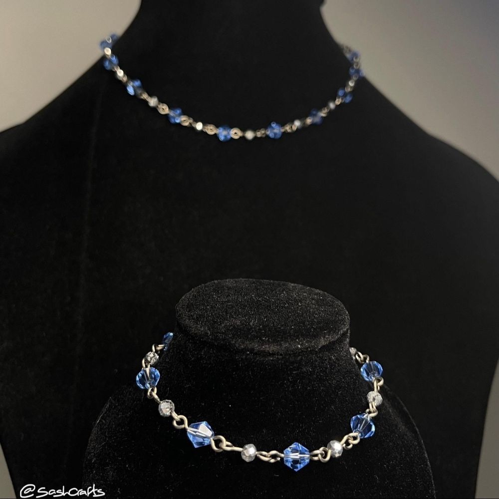 a matching blue and silver bracelet and necklace set displayed on two black velvet busts with the smaller bust and bracelet closer to the camera and in focus. the pieces alternate between 6mm bicone pale blue beads and 4mm rondelle metallic silver beads, made up with 0.8mm pure titanium wire and closed with stainless steel clasps and extension chains. 