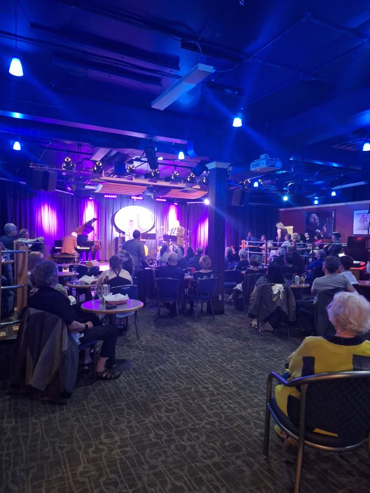 Interior of the Yardbird Suite jazz club, edmonton. A band is on stage and tables are full of guests.