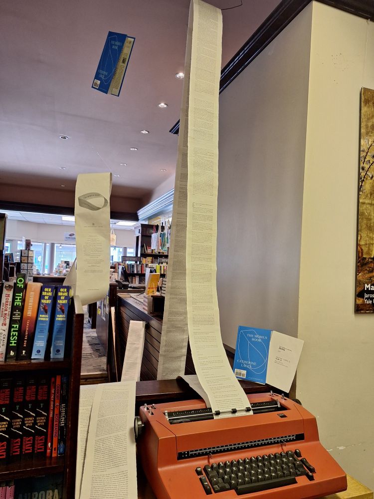 A typrwriter, a very long mobius strip made from the pages of 'The Mobius Book' by Catherine Lacey, accompanied by book covers.