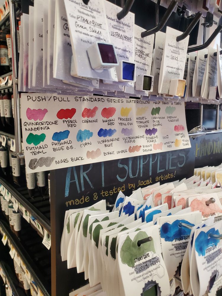 Swatch sheet of standard watercolors on display under individually available half pans of store-made watercolor. 
