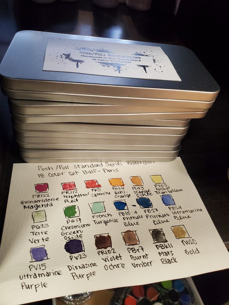 Stack of tins featuring half pans of standard colors and an accompanying swatch page.