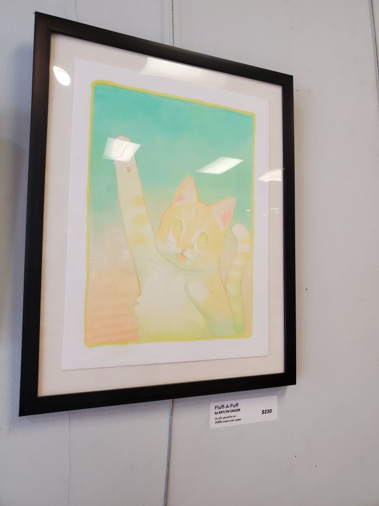 Framed painting of a yellow cat raising its paw against a blue background.