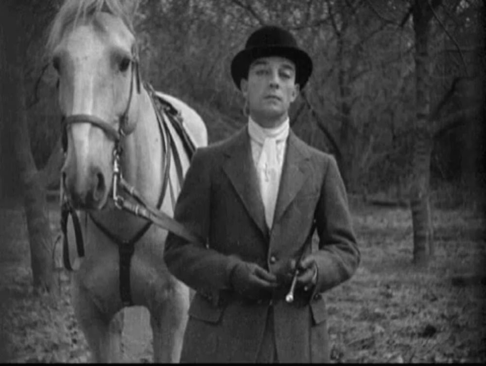 a man in a suit and bowler hat is standing next to a horse .