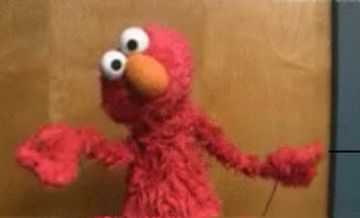 Elmo puppet raises his shoulders, as he is saying « it is what it is » or « I don’t know »