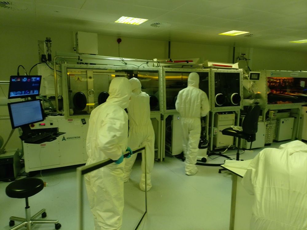 Cleanroom users dressed in their white PPE suits. One user is carrying a window to attach to the glovebox.