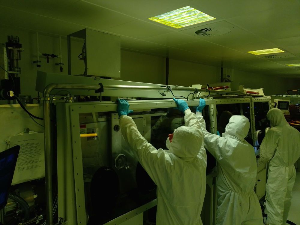 Cleanroom users dressed in their white PPE suits. They are replacing the glovebox window.
