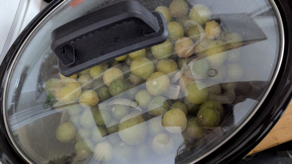 Green tomatillos, garlic and onion in a crock pot with a glass lid 