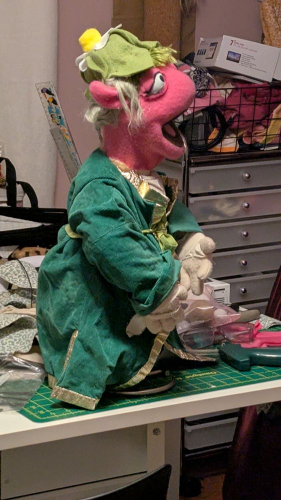 A pink fraggle like muppet with a green hat and jacket 