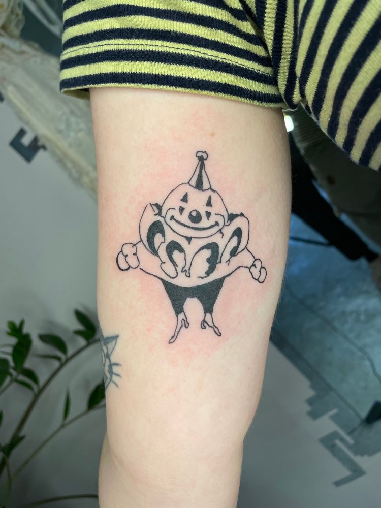 Tattoo of a small round-ish illustrative clown, on an inner bicep