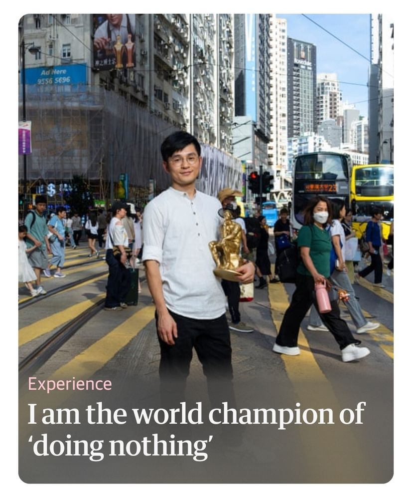 Screenshot from the Guardian. A.man stands still in a busy street holding a trophy. Headline reads 'I am the world champion of doing nothing'.