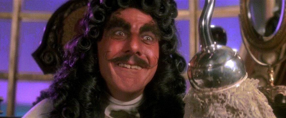 a man in a wig and mustache is smiling and holding a hook .