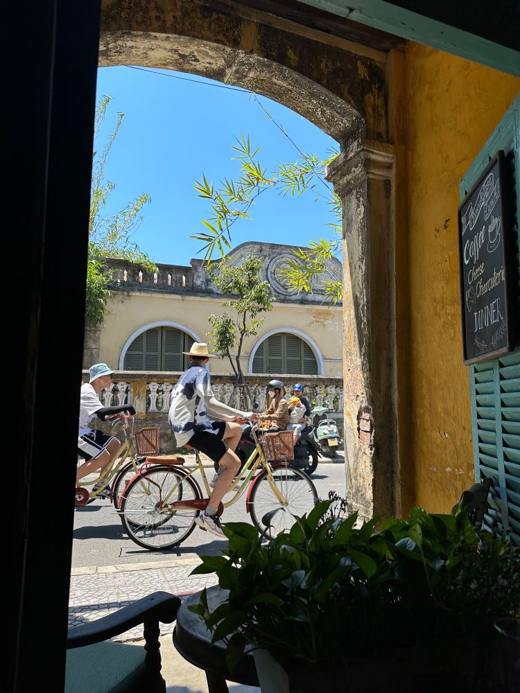 View from cafe of people passing by on bicycle and motorbike 