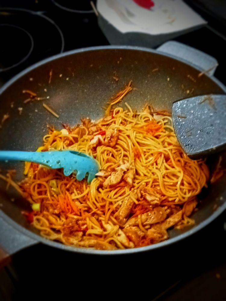 A lo mein esque stir fry in a wok. Lots of beige colors broken up by a pop of red from peppers.