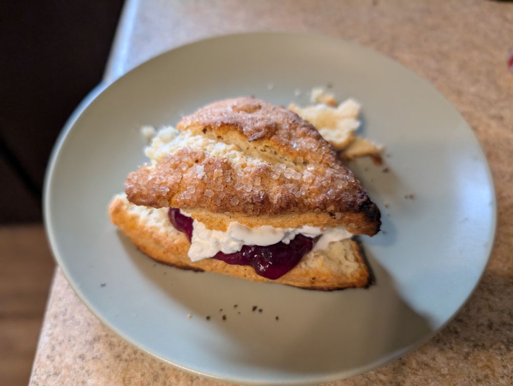 Scone, split in half, with whipped cream and raspberry jam, then stacked back together on a plate