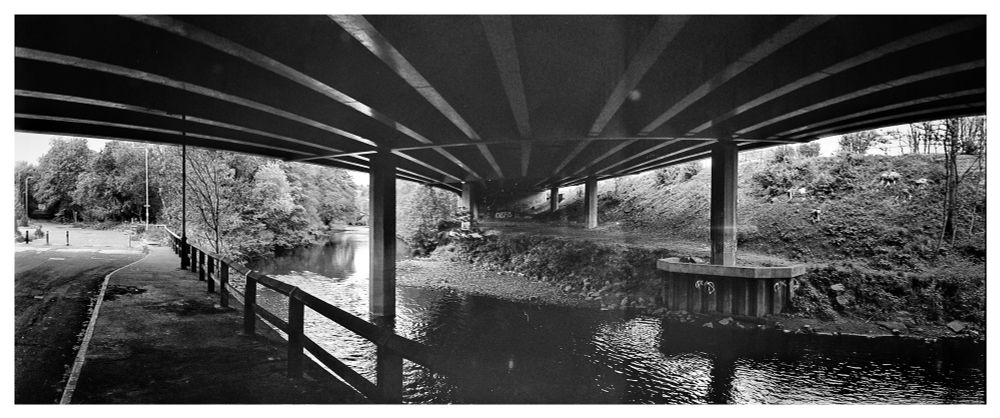 Black and white panoramic photograph takenfrom underneath the Elland bypass showing the River Calder on the right and the pavement to the left