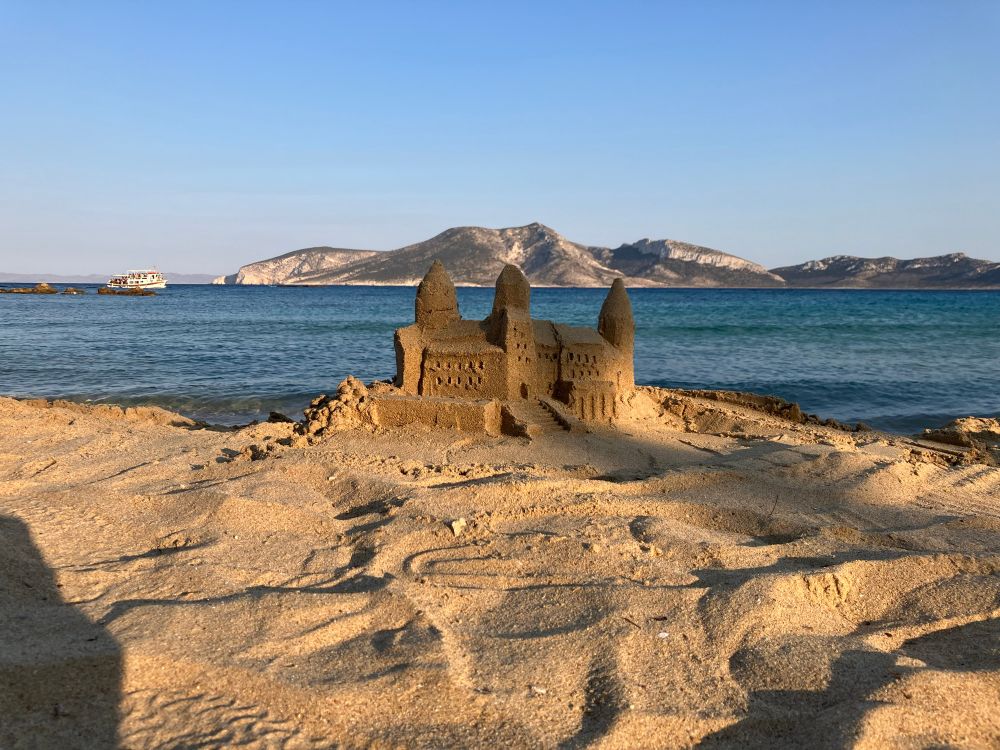 Sandburg vor Meer, im 
Hintergrund eine Insel 