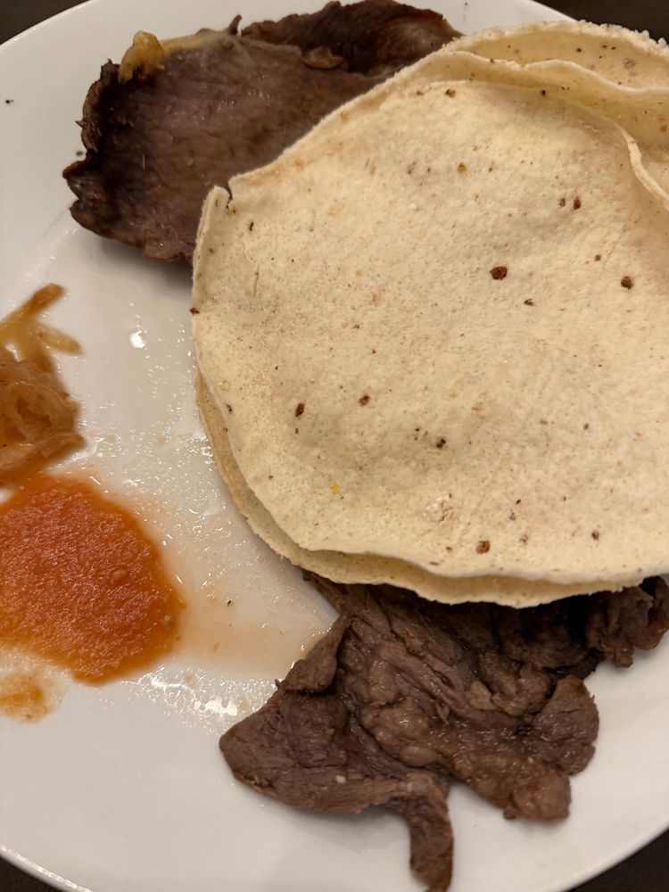 Plate of leftover steak, a red spicy sauce, tortillas and onions