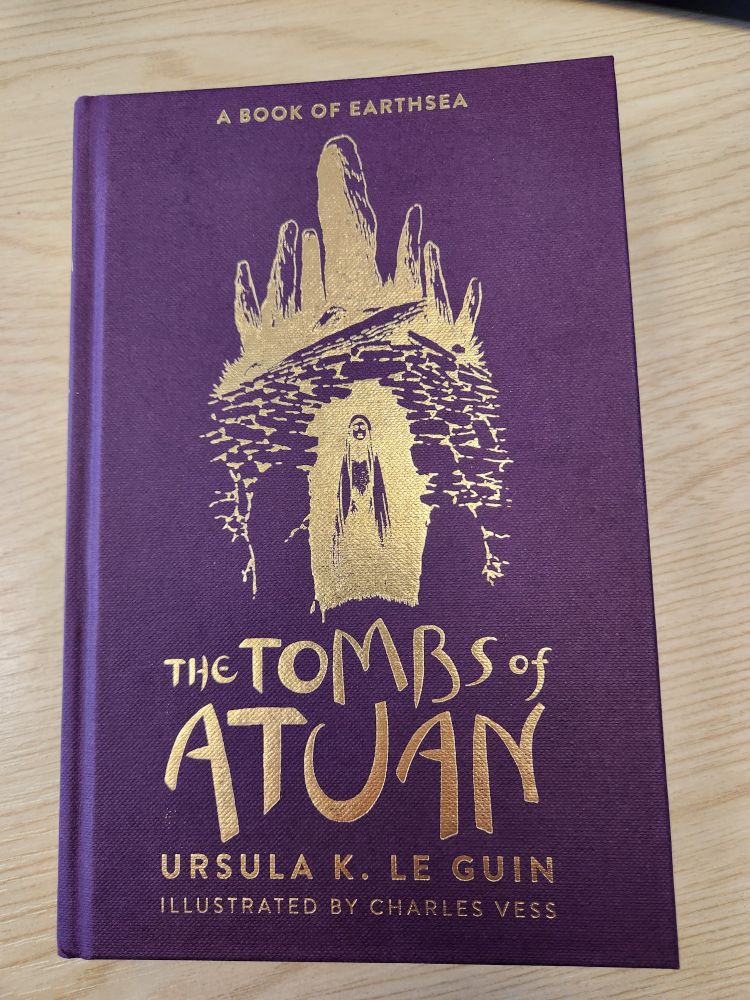 Cover of the hardback edition of The Tombs of Atuan by Ursula Le Guin. Purple cloth binding with gold lettering and illustration.