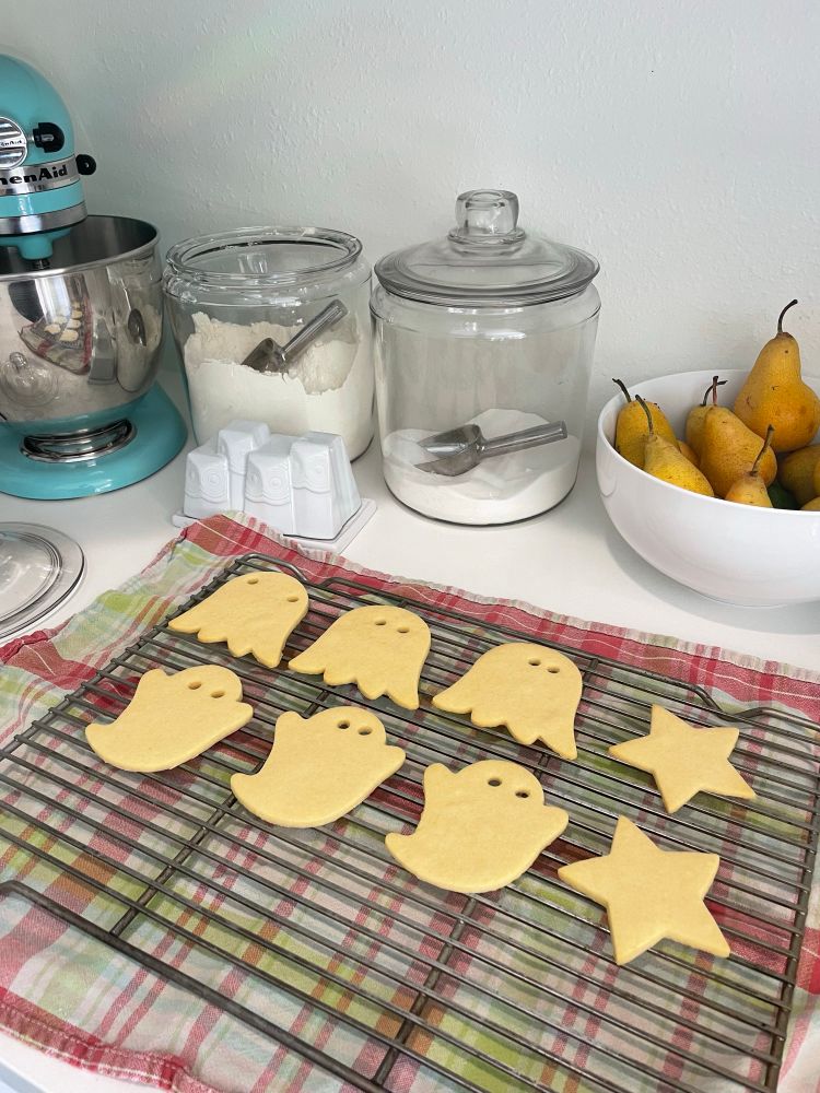 Photo of ghost shaped and star shaped cookies resting on a baking rack, with sugar and pears visible in the background.