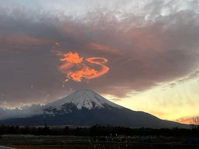 A reddish orange dragon-like sunrise cloud captured over snow- capped Mount Fuji.