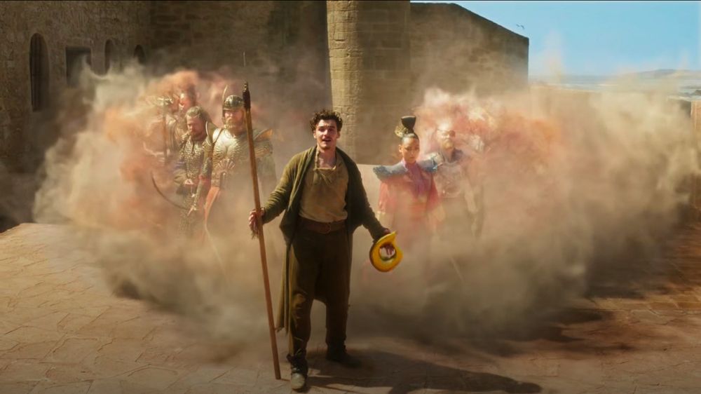 Mat Cauthon (Dónal Finn) standing at the center with his arms spread out at his sides and in his right hand holding a makeshifts Ashandarei staff and left hand holding a Golden horn. Smoke/mists appeared behind him from his left and right. Rows of The Heroes of the Horn emerged from the mists.