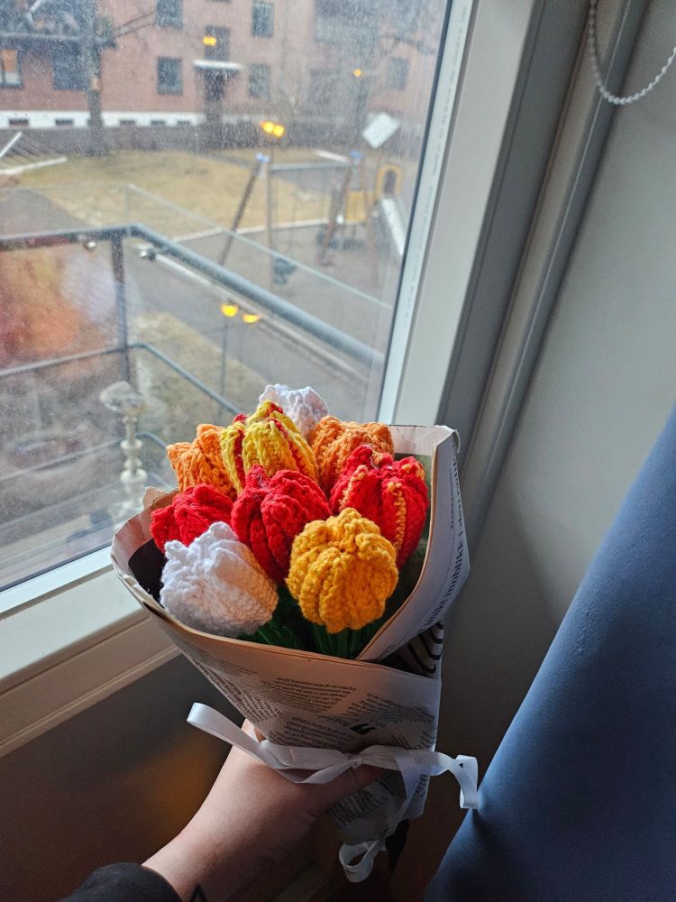 En heklet bukett tulipaner. Blomstene er rød, gule, hvite og er pakket inn i avispapir