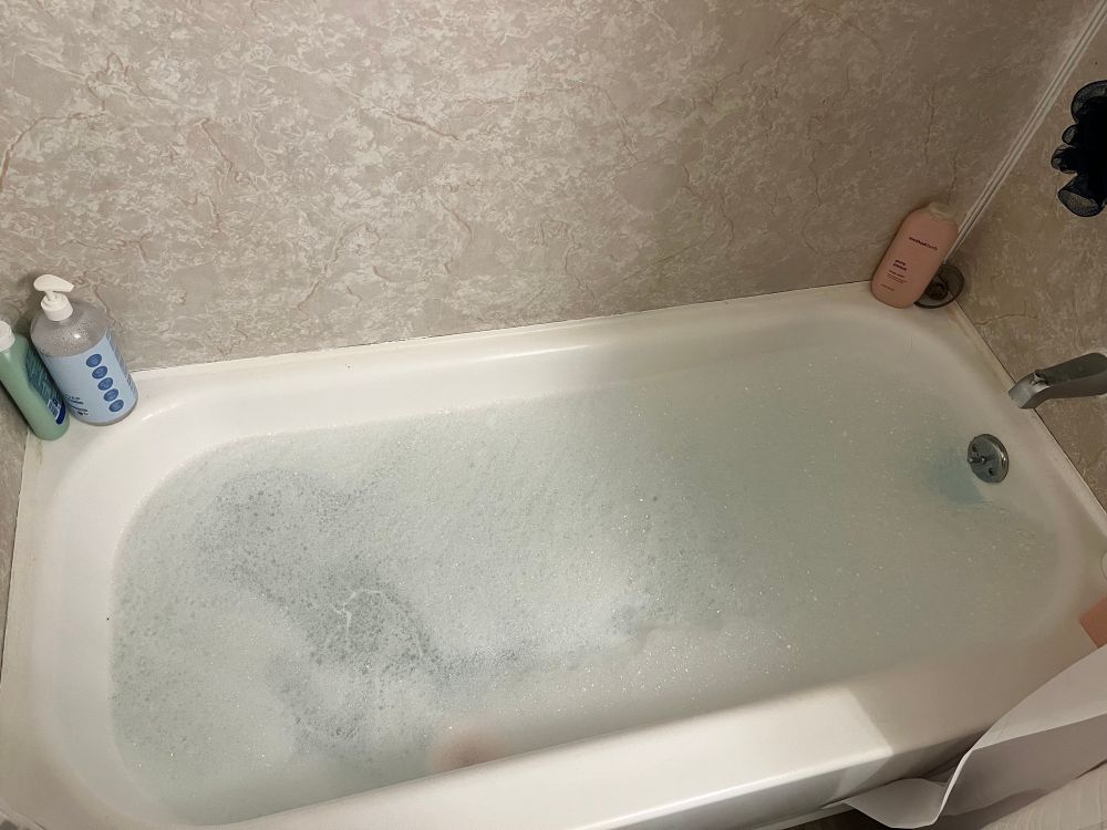 bubble bath with blue-tinted water and a still-dissolving pink bath bomb in the front left corner of the tub