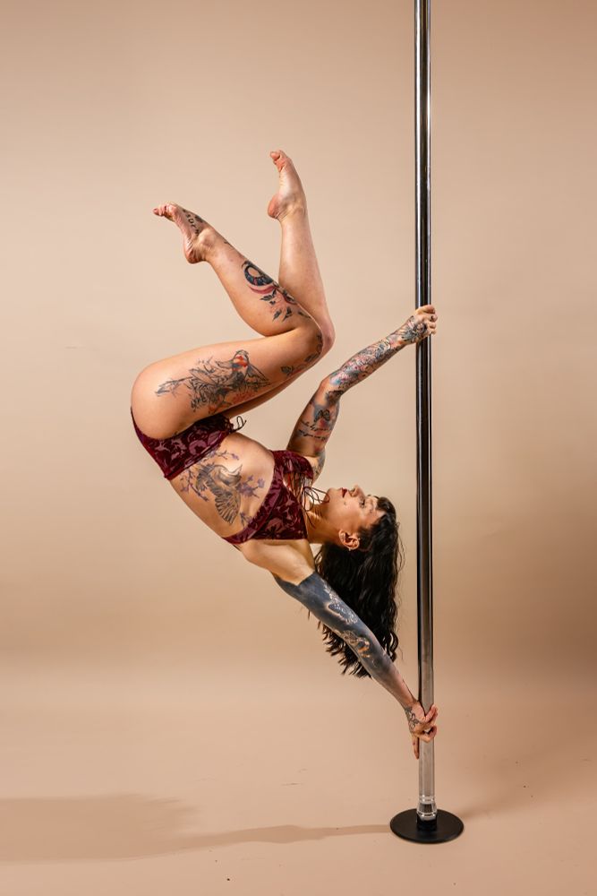 Me doing a handspring with both legs bent. I am looking up. My hands are positioned in true grip. I am wearing a red floral pole set and the background is beige.