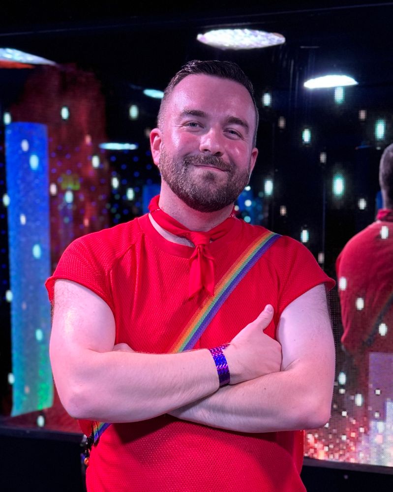 A man wearing a red jersey shirt with a bag with a rainbow strap. It’s me I’m the man 
