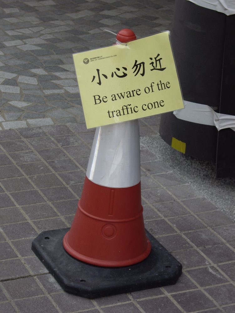 A traffic cone with a sign on it reading 'please be aware of the traffic cone' in English and Cantonese.