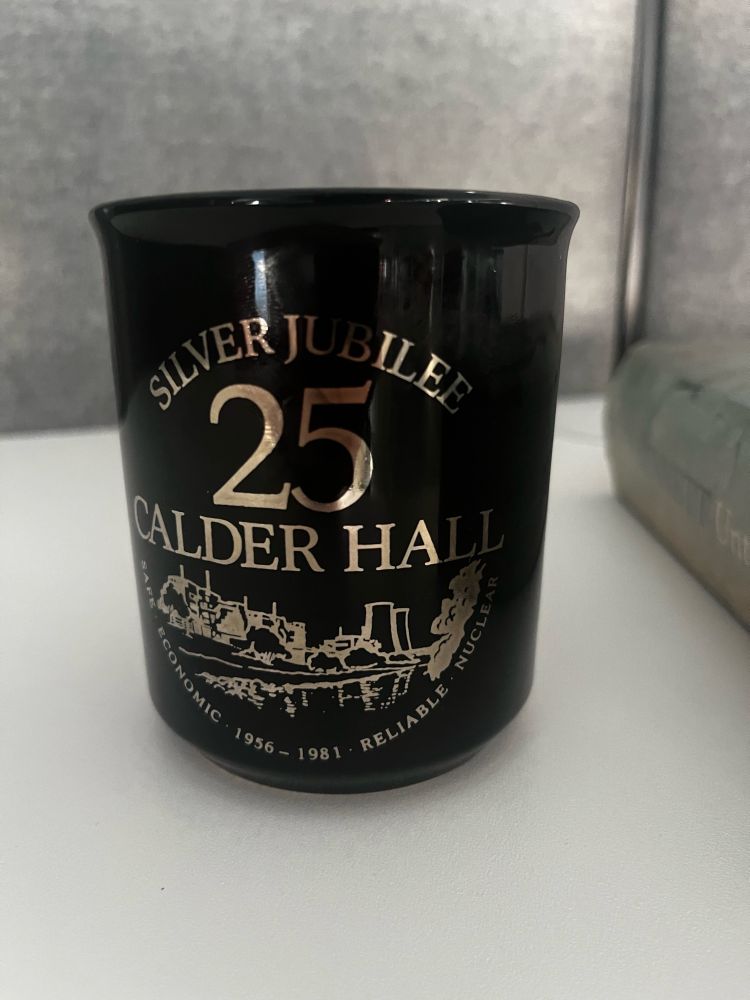 A black mug with gold inscription and image celebrating the 25th anniversary of Calder Hall nuclear power plant from 1981.