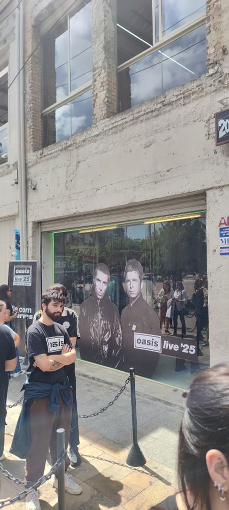 Fachada da loja do Oasis em São Paulo. Uma vitrine adesivada com uma foto preta e branca dos irmãos Gallagher. 