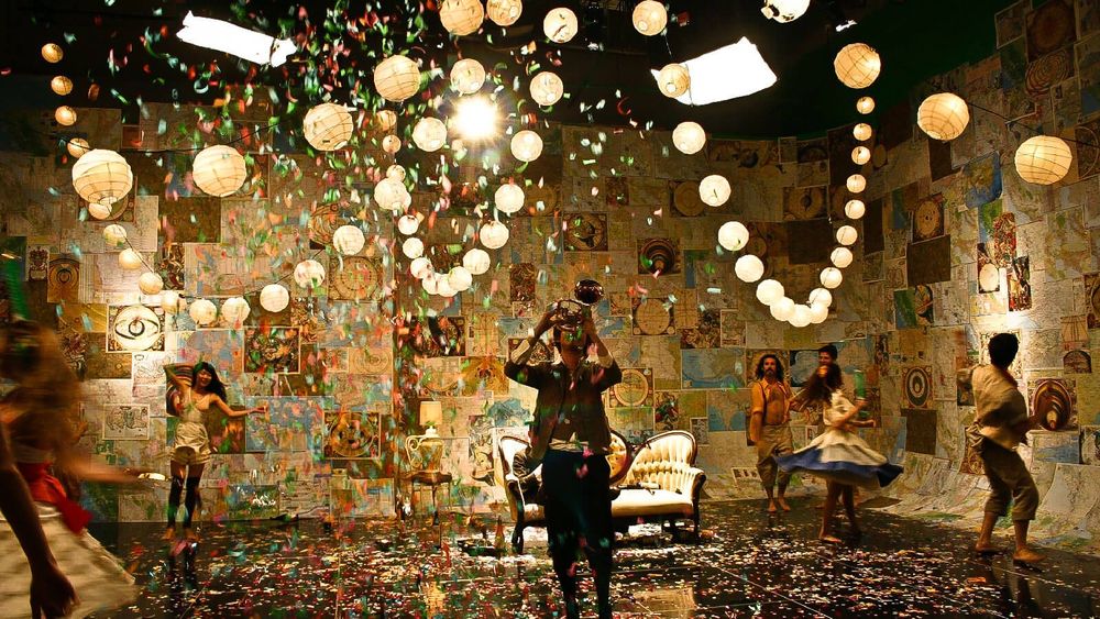 Still from the music video of the song “Elephant Gun” by Beirut featuring a crowd of bright young things shabbily dressed and dancing around a Baroque chaise while confetti rains down. One of them is playing a trumpet.
