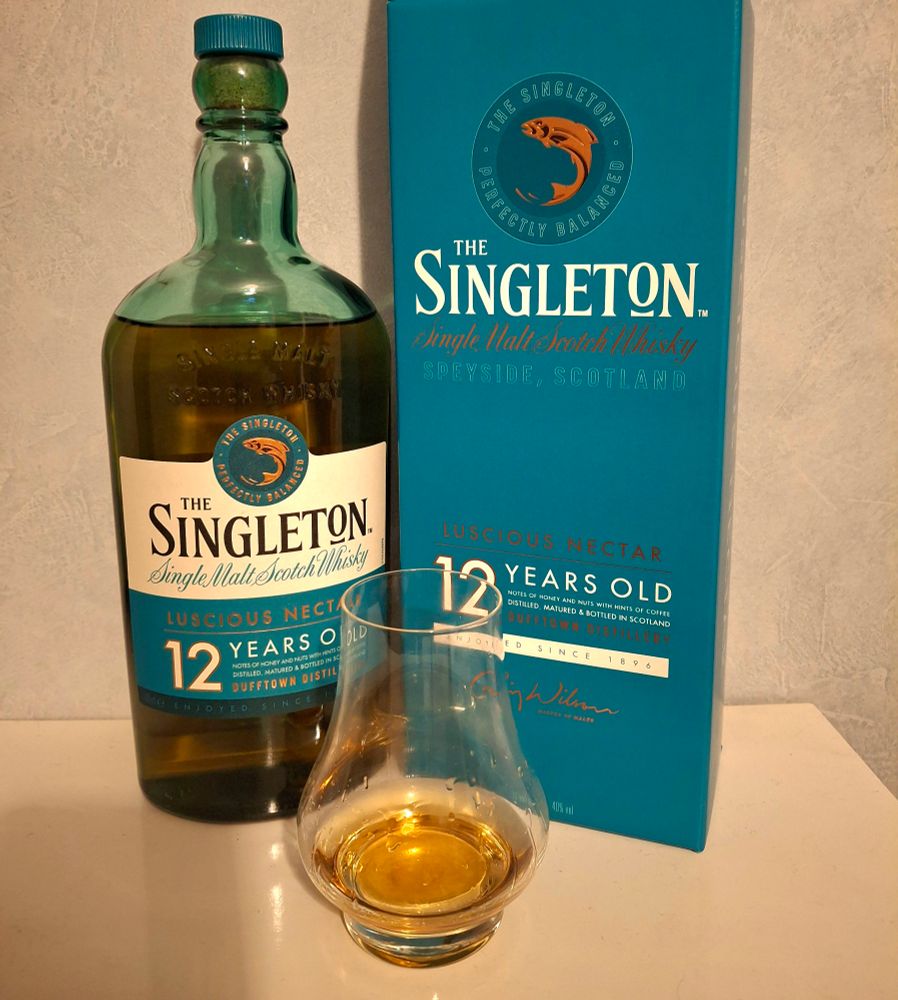 Photo of a bottle of Singleton single malt whisky alongside its cardboard case and a near empty glass
