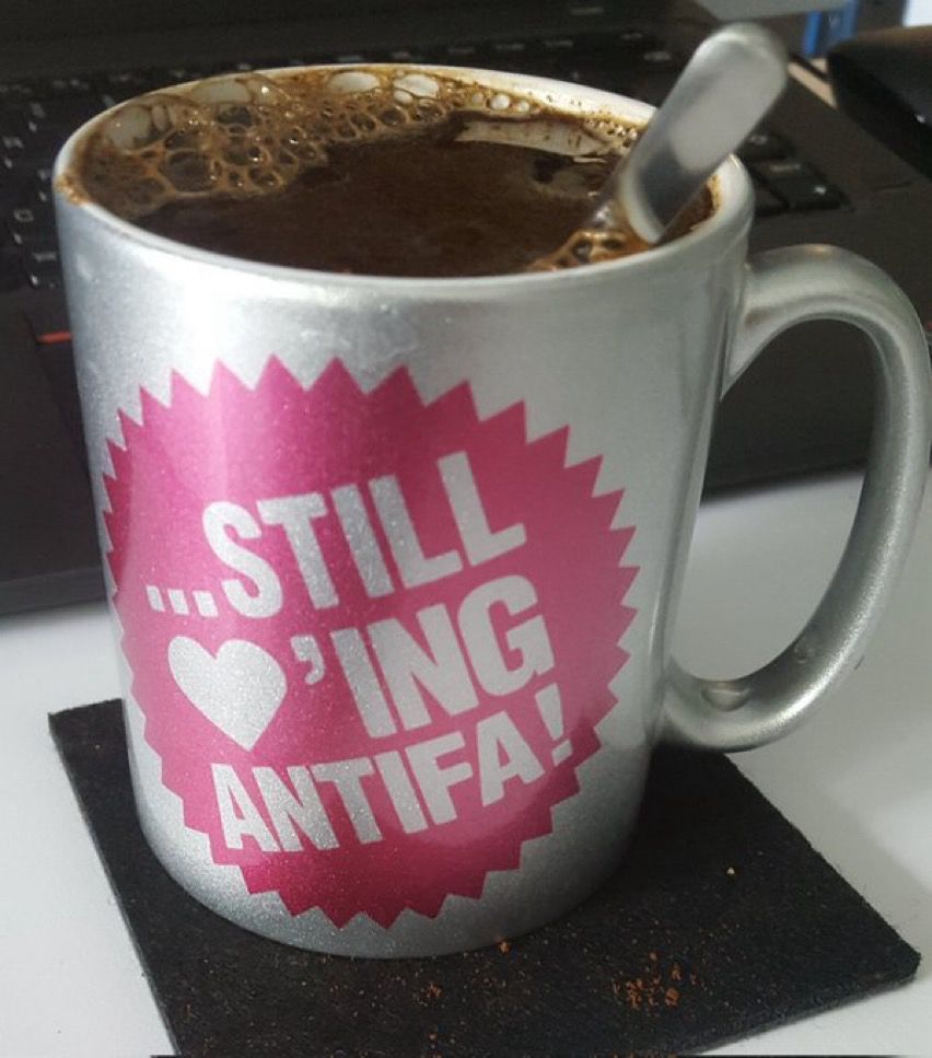Silberfarbene Kaffeetasse mit Aufschrift:
Still loving antifa!