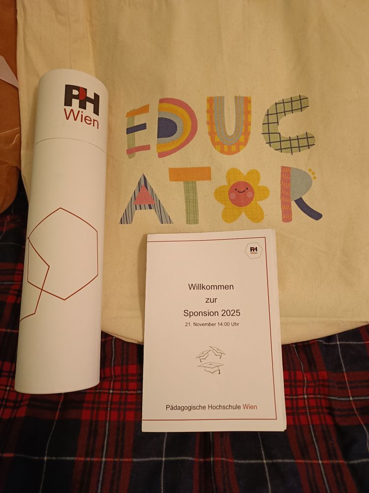 eine Stofftasche mit Aufdruckt "Educator", eine weiße Festfolle mit dem Logo der PH Wien, ein A5 Programmheft zur Feier