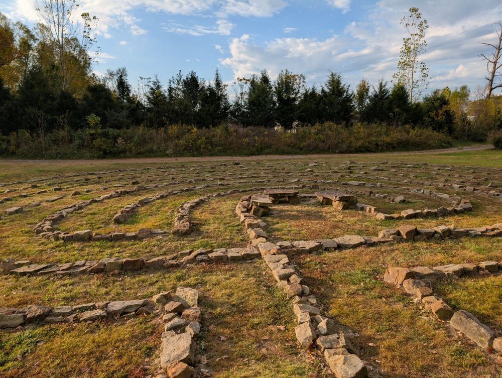 Photo of a stone labyrinth with a line of trees behind it.