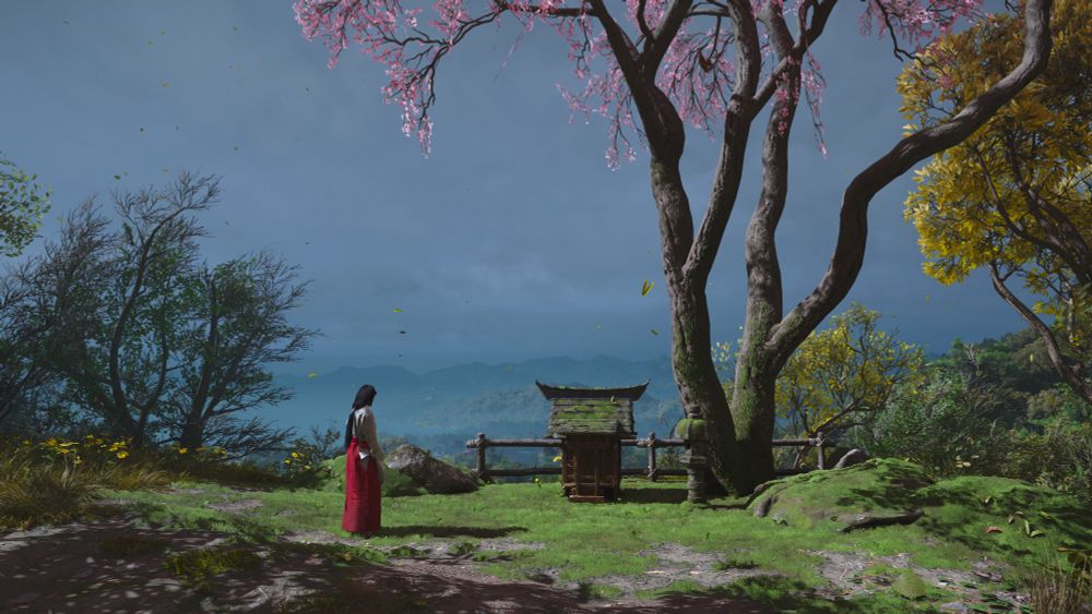 In a landscape scene dominated by green grass, distant Payne’s grey clouds and hills, and a blooming pink cherry blossom tree, a tiny figure of a woman in red mourns by a small wooden shrine. 