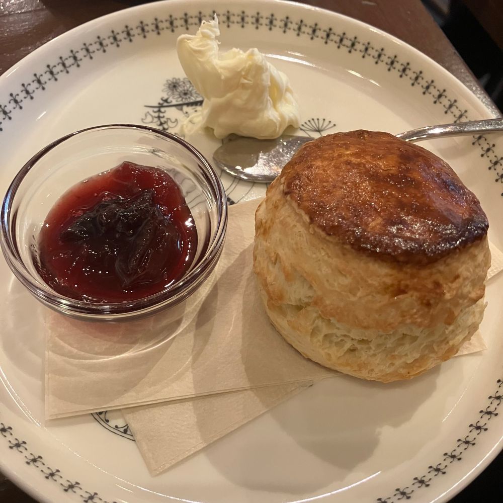 右下にスコーン、左隣に赤紫色のジャムが透明な器に入っている。上にクロテッドクリームが盛っている。
